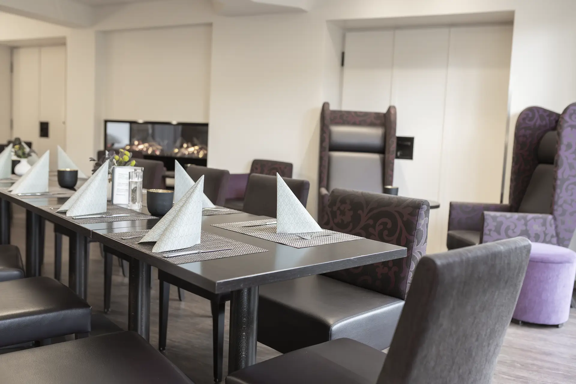 Gedeckter Restauranttisch mit weißen Servietten und gepolsterten Sitzbänken.