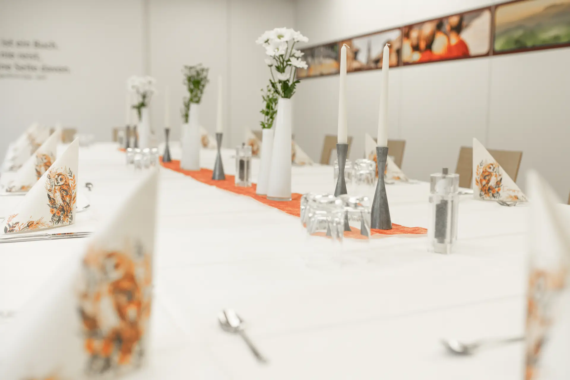 Lange Festtafel mit Blumenvasen, Gläsern und orangefarbenem Tischläufer.