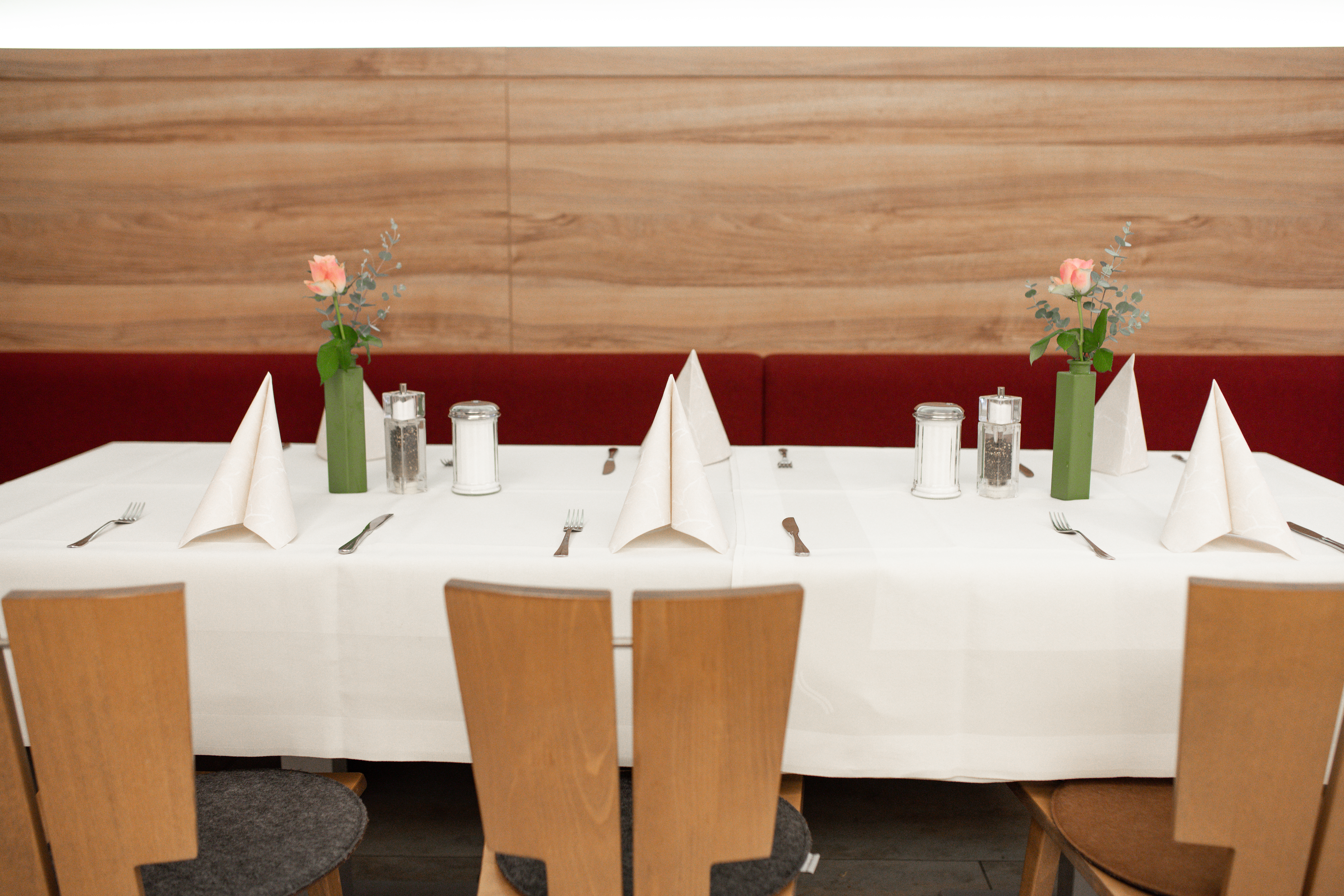 Gedeckter Restauranttisch mit Blumen und gefalteten Servietten vor einer Holzbank.