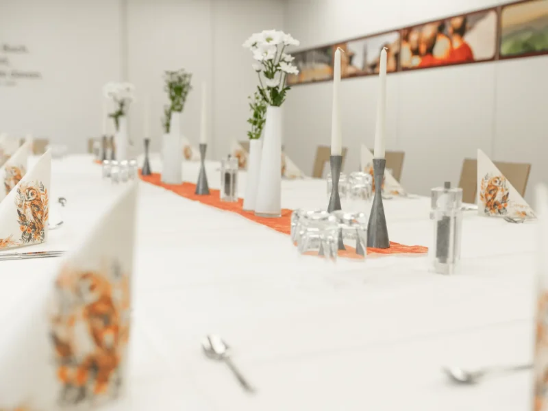 Lange Festtafel mit Blumenvasen, Gläsern und orangefarbenem Tischläufer.