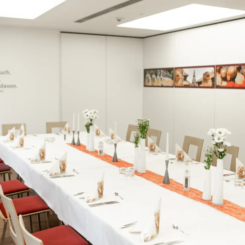 Heller Veranstaltungsraum mit festlich gedeckter langer Tafel.