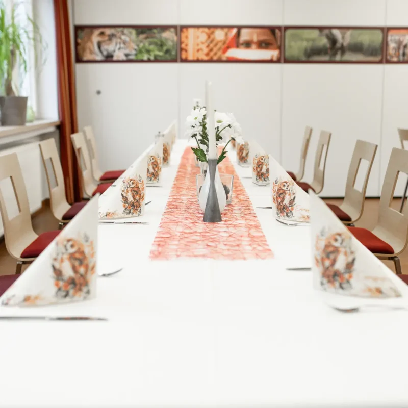 Lange gedeckte Festtafel mit Blumen und orangefarbenem Tischläufer.