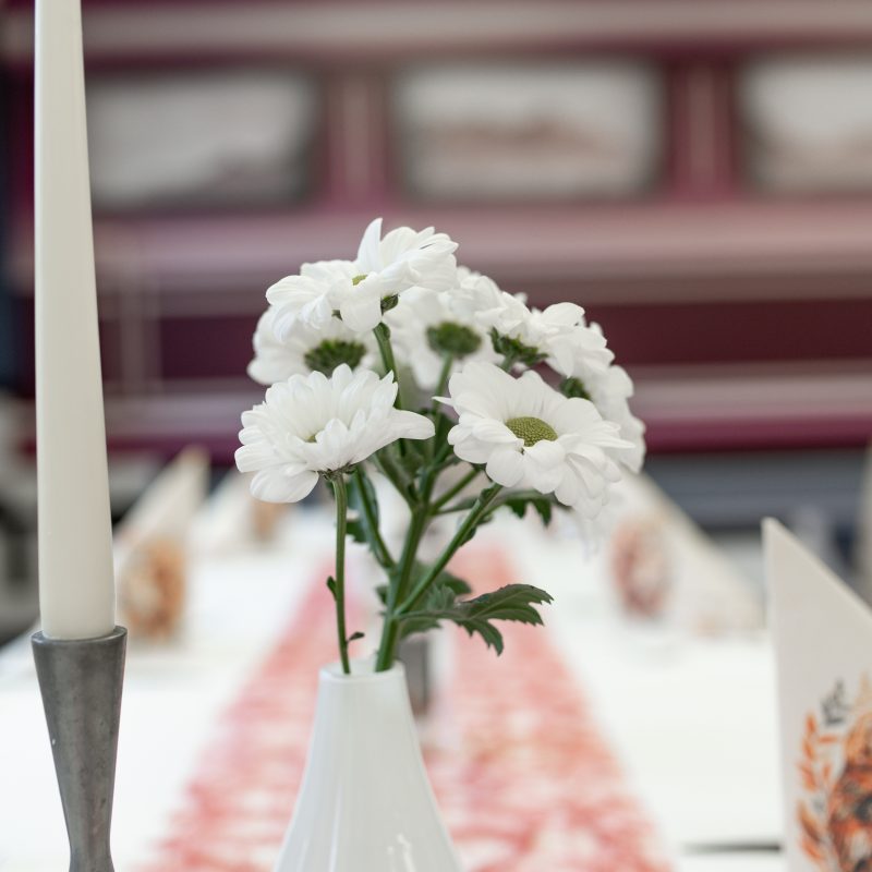 Weiße Blumen in einer kleinen Vase auf einem gedeckten Restauranttisch.