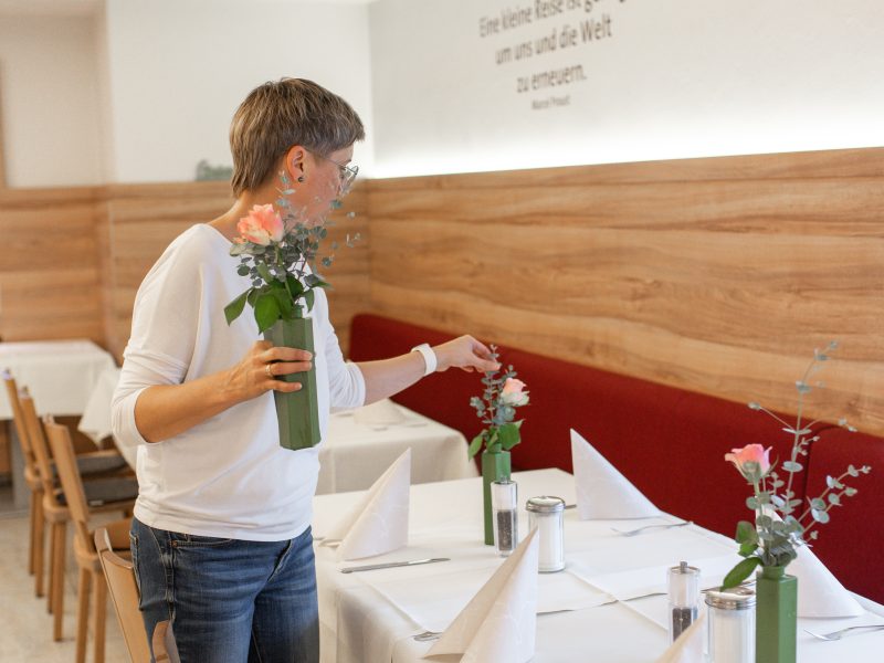 Mitarbeiterin dekoriert einen festlich gedeckten Tisch mit Blumen.