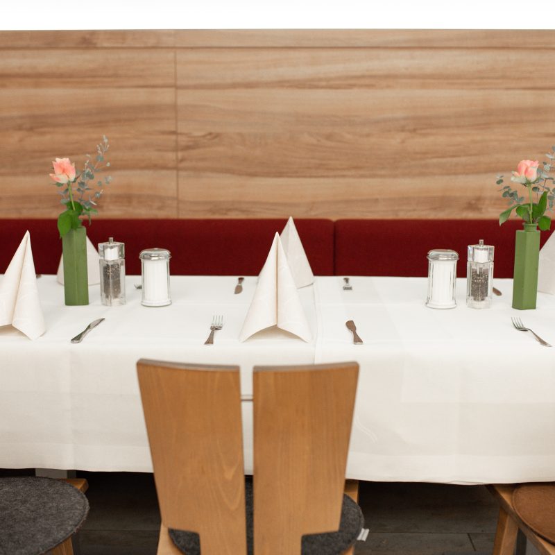 Gedeckter Restauranttisch mit Blumen und gefalteten Servietten vor einer Holzbank.