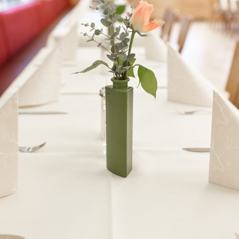 Rosafarbene Rose in einer grünen Vase auf einem gedeckten Tisch.