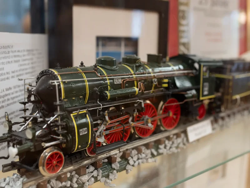 Detailreiches Modell einer schwarzen Dampflokomotive mit roten R&auml;dern in einer Vitrine.