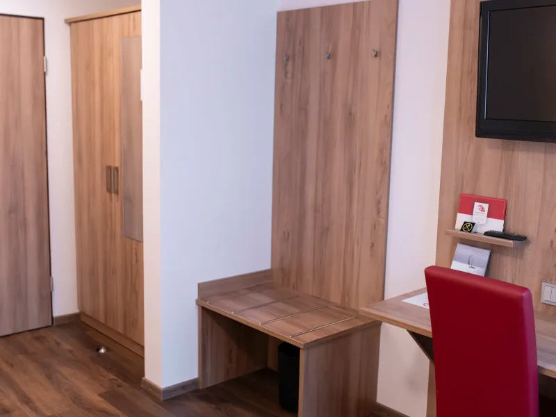 Holzschrank und Garderobenbereich in einem hell eingerichteten Hotelzimmer.