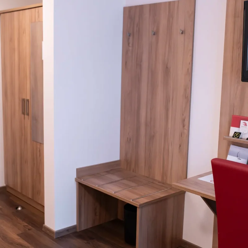Holzschrank und Garderobenbereich in einem hell eingerichteten Hotelzimmer.