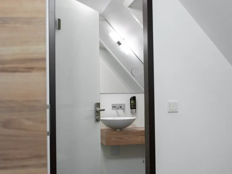 Ge&ouml;ffnete Hotelzimmert&uuml;r mit Blick in einen hellen Eingangsbereich und auf ein Waschbecken.