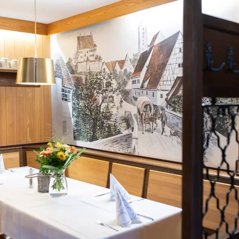 Restaurant mit Holzmöbeln, historischen Wandbildern und gedeckten Tischen.