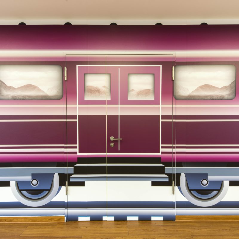 Frontansicht eines weinroten Eisenbahnwaggons mit mittiger Tür und Fenstern.