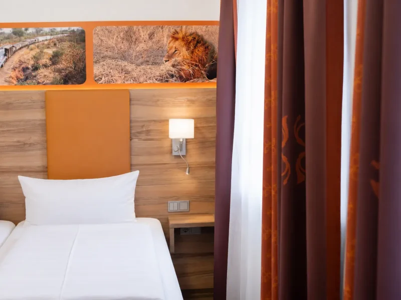 Ausschnitt eines Hotelbetts mit orangefarbenem Kopfteil und Wandleuchte.