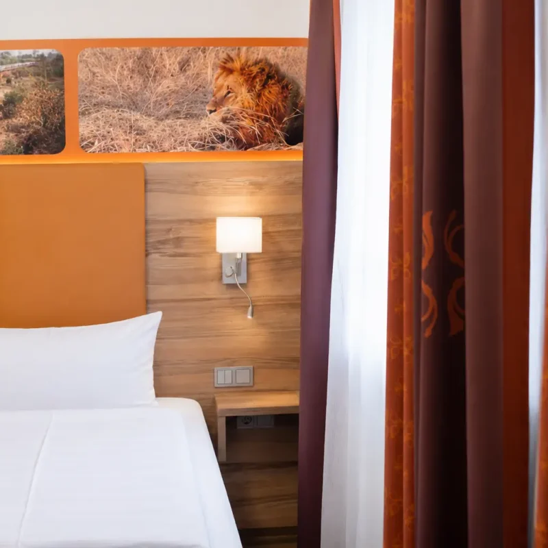 Ausschnitt eines Hotelbetts mit orangefarbenem Kopfteil und Wandleuchte.