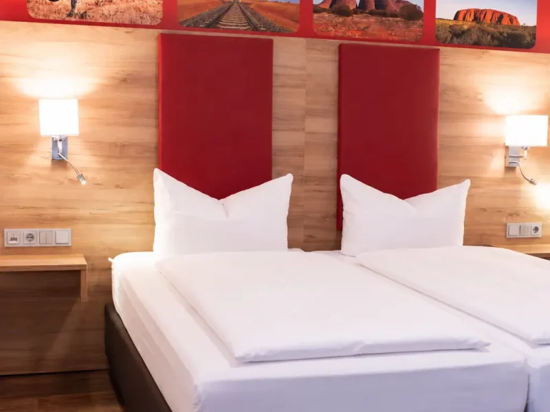 Doppelbett mit roten Kopfteilpolstern, wei&szlig;en Kissen und zwei Wandleuchten.