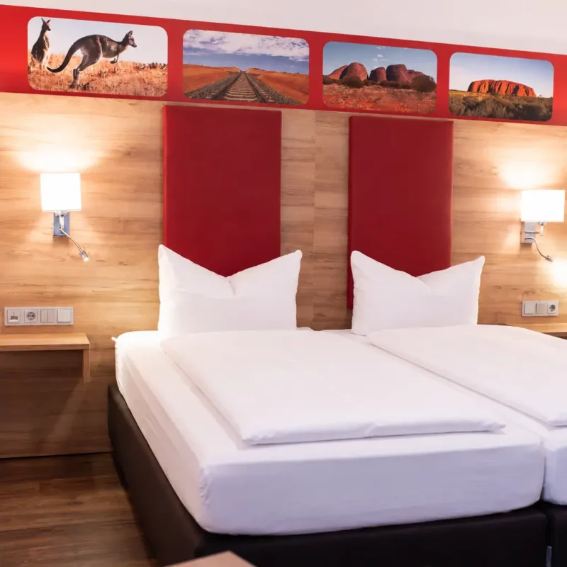 Doppelbett mit roten Kopfteilpolstern, wei&szlig;en Kissen und zwei Wandleuchten.