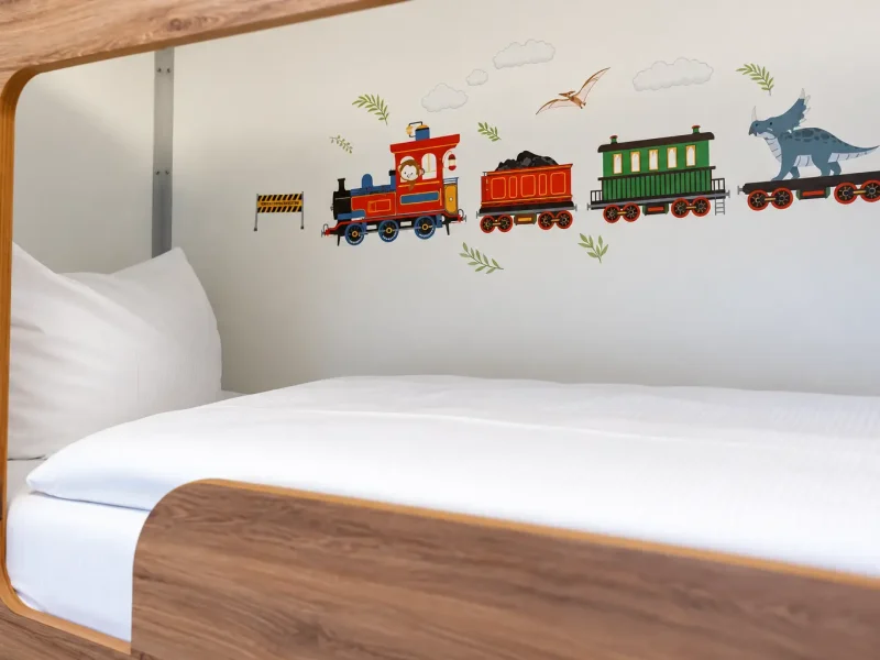 Helles Bett mit bunter Eisenbahn als Wanddekoration.