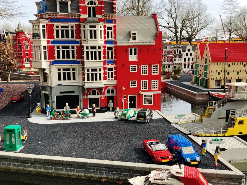 Buntes Miniaturgebäude mit roten Fassaden und kleinen Fahrzeugen in einer Modelllandschaft.