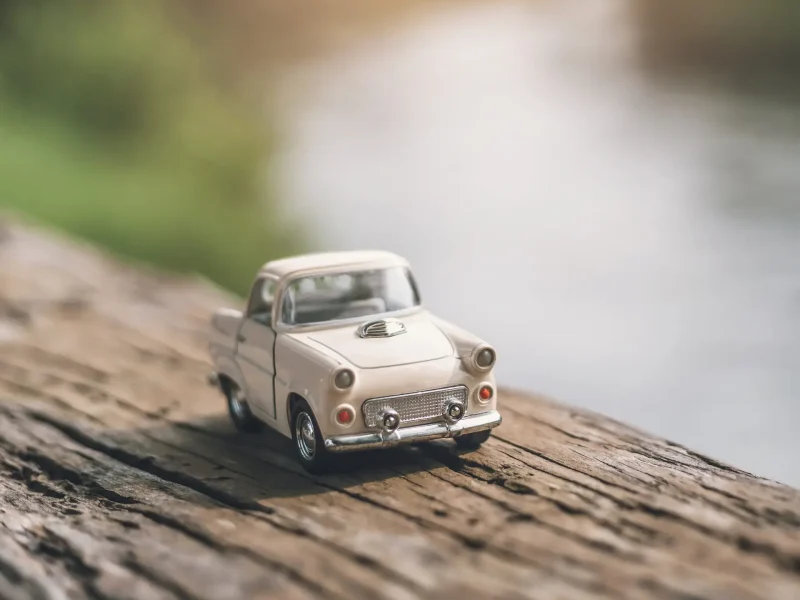 Kleines helles Modellauto vor einer unscharfen gr&uuml;nen Landschaft.